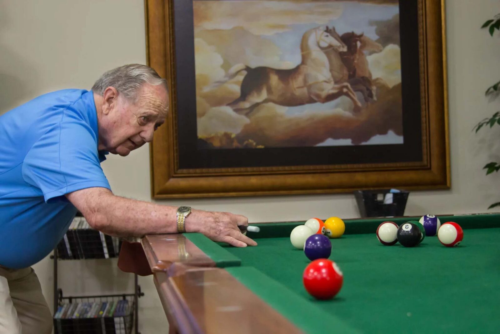 Elderly man playing pool, colorful balls on green table.