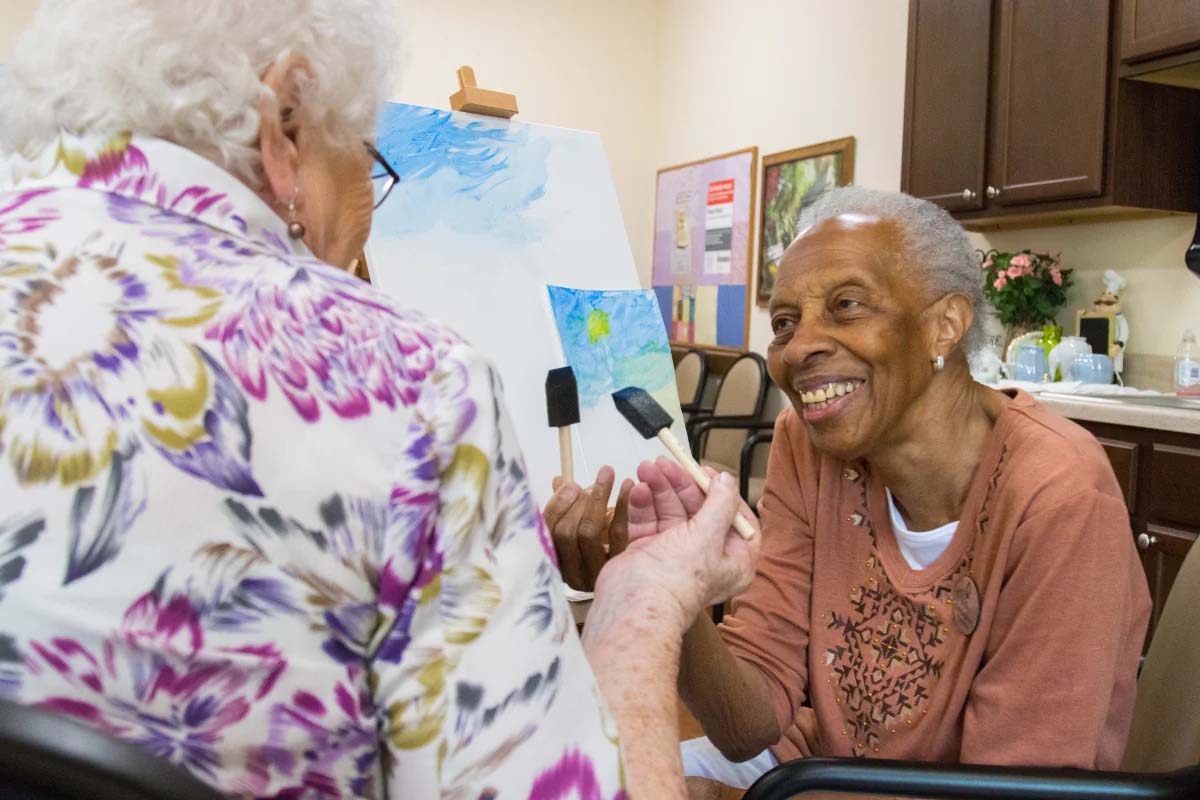 Two women enjoying painting together, sharing smiles and laughter.
