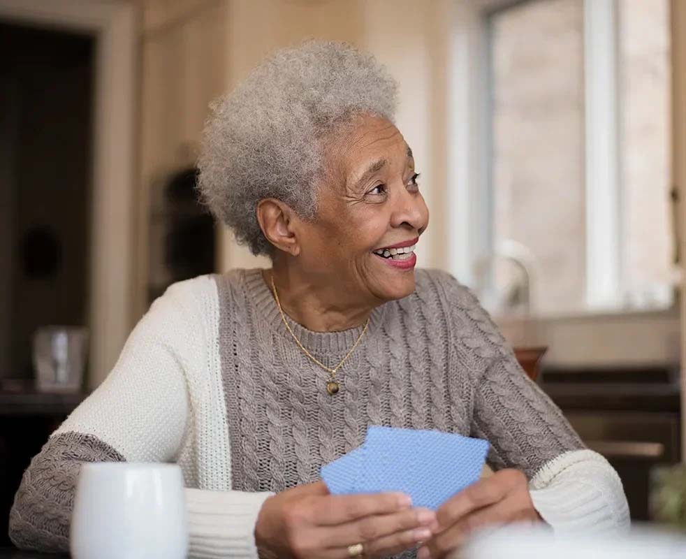 Smiling elderly woman holding cards, cozy indoor setting.